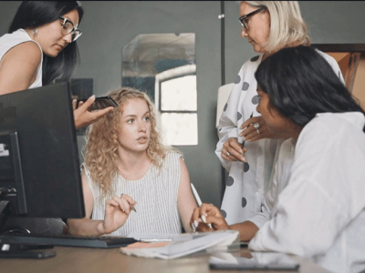 four women discussing around computer