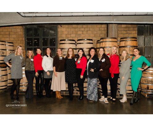 Group of women standing in front of whisky barrells at a holiday party.