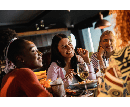 Group of young female friends having fun in restaurant, talking and laughing while dining at table.