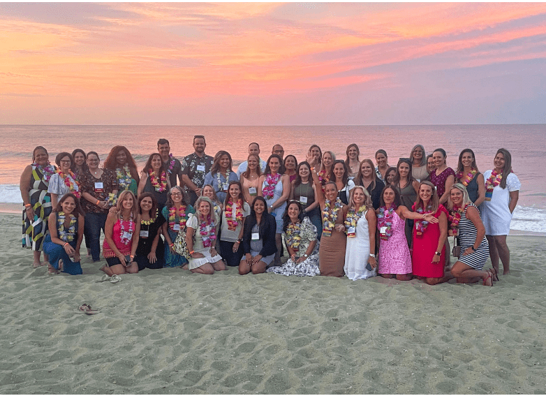 group of people posing for a picture on the beach at sunset