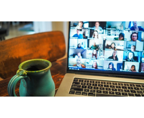Close up of coffee mug and laptop on a virtual meeting with a grid of diverse faces.