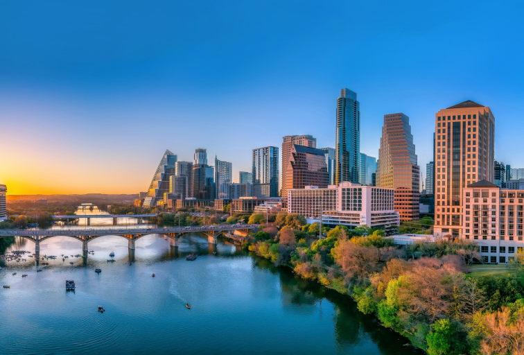 Austin, Texas- Panoramic cityscape and Colorado River against the sunset sky. There are bridges over the river with boats under and a view of the skyscrapers on the sides.