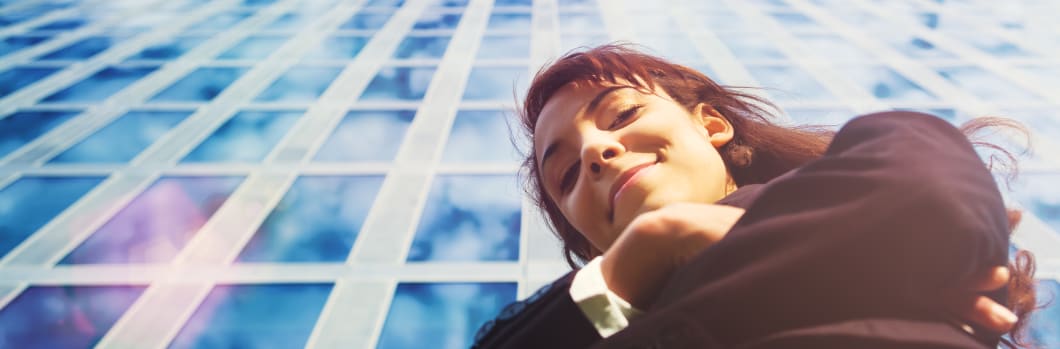 businesswoman looking down at camera in front of glass skyscraper