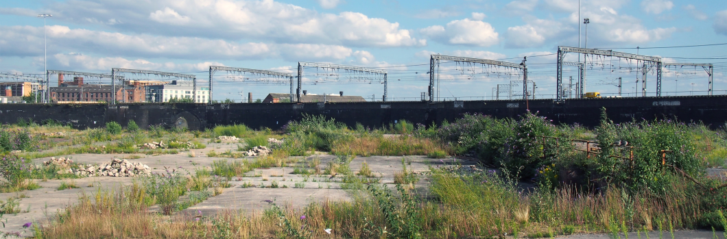 a large unused urban brownfield site with open land covered in cracked overgrown concrete awaiting development in leeds england