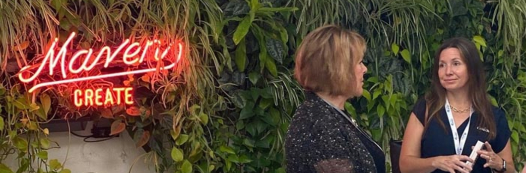 Two women talking in front of a "Maven" neon sign