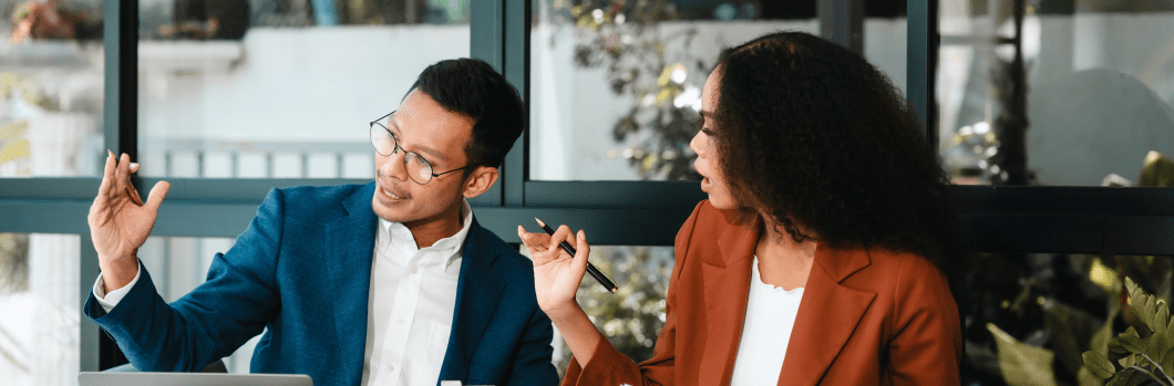 Attractive Asian businessman and African American female real estate and land investor talk discussing together on table with laptop and small building model. Reserve fund.
