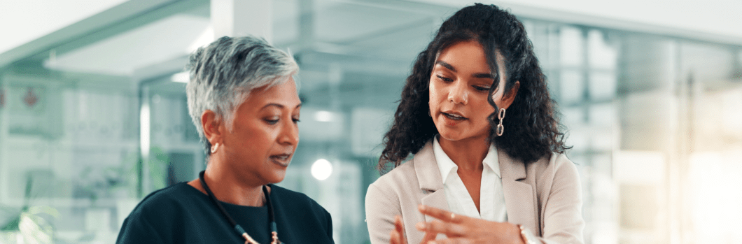 Two women looking at a tablet together; one is younger, suggesting a mentoring relationship.
