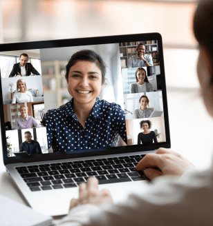 Woman sit at desk looking at computer screen where collage of diverse people webcam view. Indian ethnicity young woman lead video call distant chat, group of different mates using videoconference app