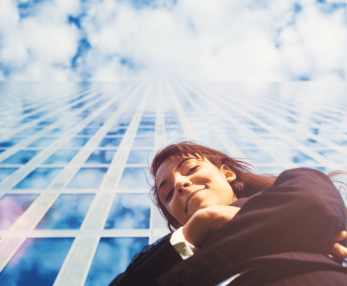 businesswoman looking down at camera in front of glass skyscraper