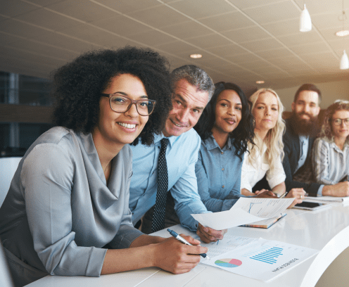 Portrait of a smiling group of diverse corporate colleagues standing in a row together at a table in a bright modern office