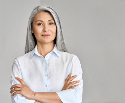 Stylish confident adult 50 years old Asian female psychologist standing arms crossed looking at camera at gray background. Portrait of sophisticated grey hair woman advertising products and services.