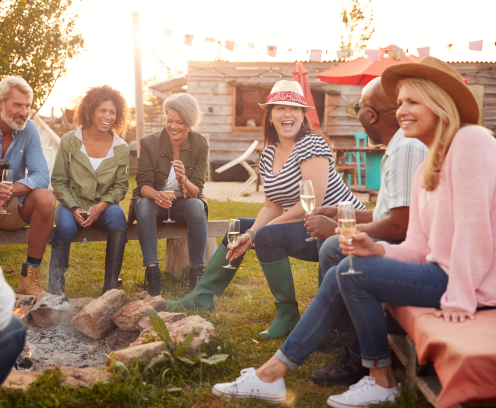 Group Of Mature Friends Sitting Around Fire And Drinking At Outdoor Campsite Bar