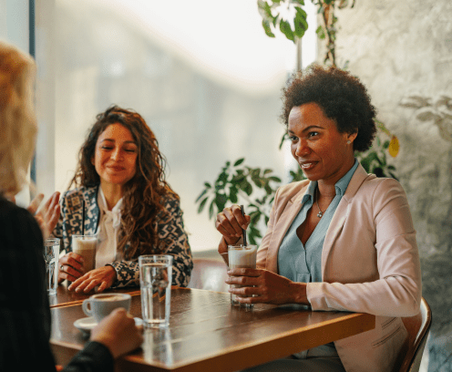 Three empowered beautiful women in elegant suits sitting at the cafe, having fun and socializing over drinks