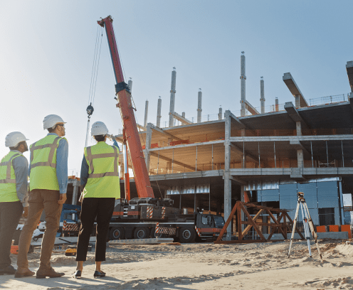 Diverse Team of Specialists Inspect Commercial, Industrial Building Construction Site. Real Estate Project with Civil Engineer, Investor and Worker. In the Background Crane, Skyscraper Formwork Frames