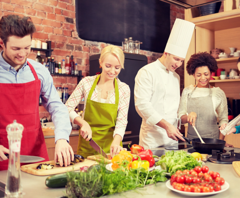 cooking class, culinary, food and people concept - happy group of friends and male chef cook cooking in kitchen