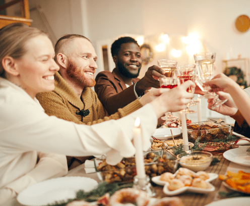 Multi-ethnic group of people raising glasses sitting at beautiful dinner table celebrating Christmas with friends and family, copy space