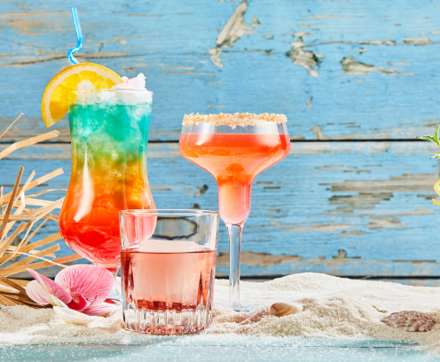 Exotic summer drinks on white beach sand, viewed from the front against blue wooden background