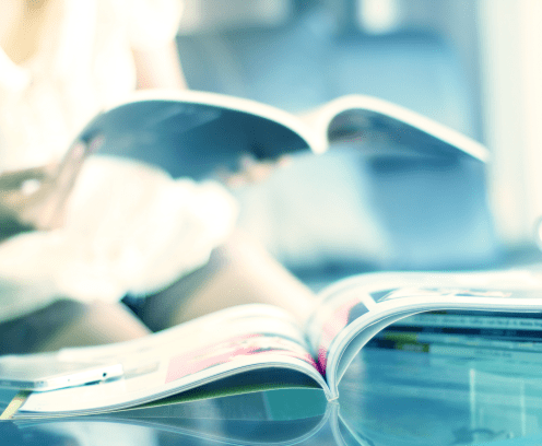 magazine open on table with woman reading magazine in the background