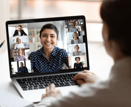 Woman sit at desk looking at computer screen where collage of diverse people webcam view. Indian ethnicity young woman lead video call distant chat, group of different mates using videoconference app