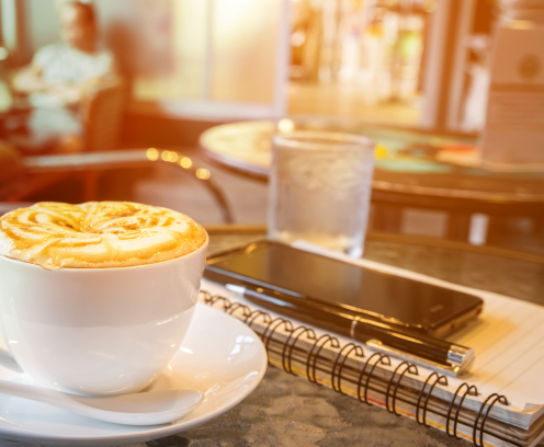 coffee cup on table with notebook, pen, smartphone, cafe