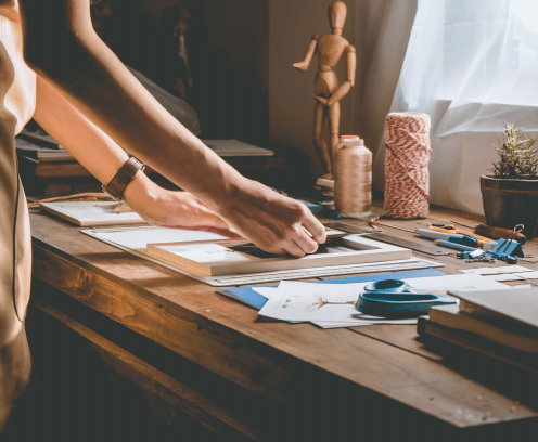 Beautiful woman hand crafting book at the tabletop with stationery. Stylish craftswoman with stationery work at his hipster workstation.