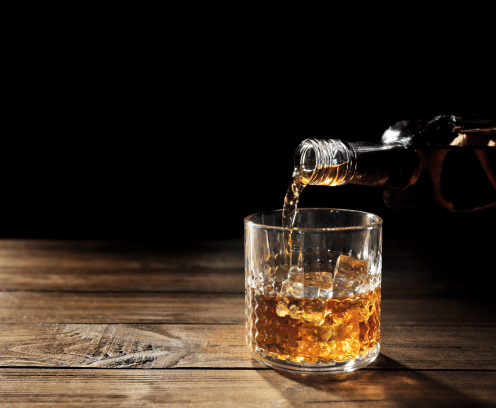 Pouring whisky into glass on wooden table closeup