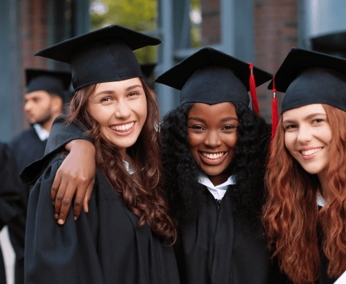 Happy group of mature students on graduation day embracing with each other. Three best girl friends in academic gowns and caps hugging in front of the camera