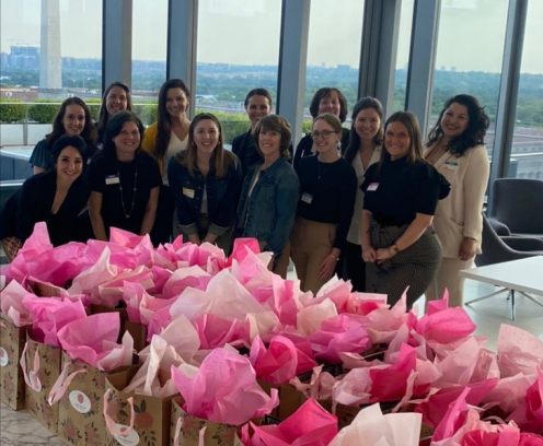 Group of women behind table of gift bags with pink tissue.