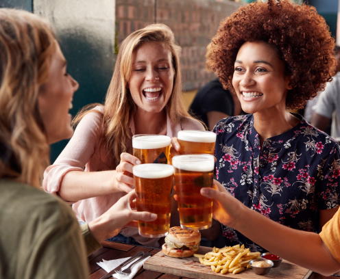 Four women at a restaurant toasting with beer