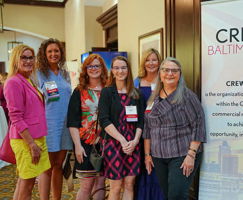 CREWBaltimore gals in a conference center standing next to CREWBaltimore sign