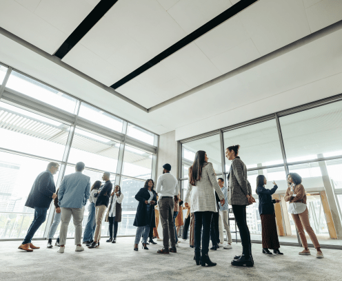 Businesspeople attending a corporate event, networking and engaging in discussions in a large, modern, bright office space.