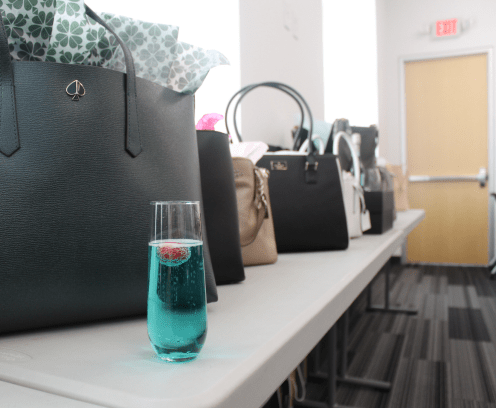 blue drink in front of a line up of women's handbags