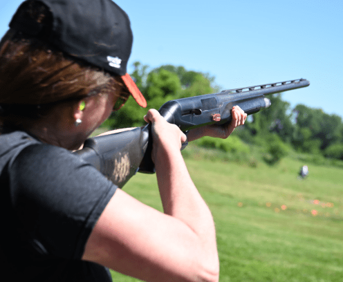 woman in baseball hat holding a gun and shooting at clay