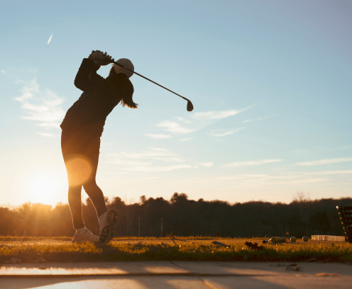 Young junior golfer practicing in a driving range with beautiful sunset light in winter.