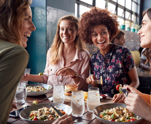 Four Young Female Friends Meeting For Drinks And Food Making A Toast In Restaurant