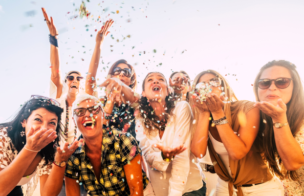 People having fun in party celebration friends concept - group of young and adult women all together laughing blowing coloured confetti - friendship and love for lifestyle with mixed active generations