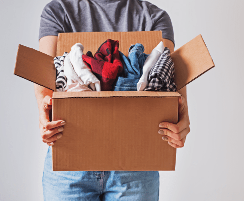Unrecognizable woman holding box with clothes in it. close-up. Clothing donation.
