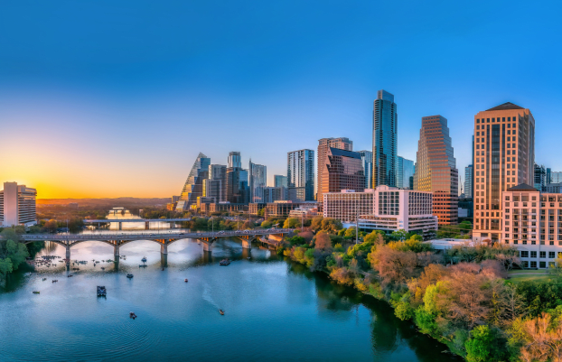 Austin, Texas- Panoramic cityscape and Colorado River against the sunset sky. There are bridges over the river with boats under and a view of the skyscrapers on the sides.
