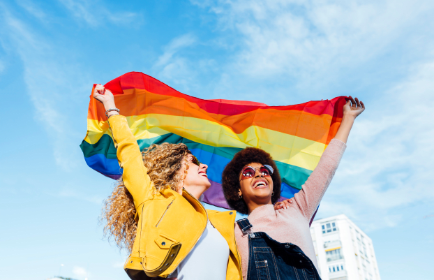Two women friends hanging out in the city waving LGBT with pride flag