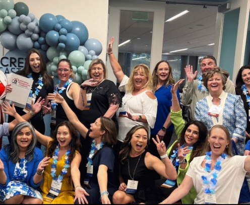 Happy people smiling in front of a CREW East Bay sign with blue balloons
