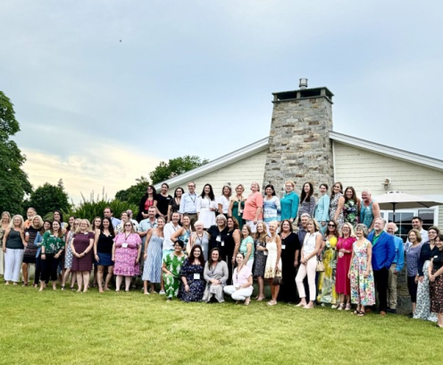 group of men and women standing in front of a tan house