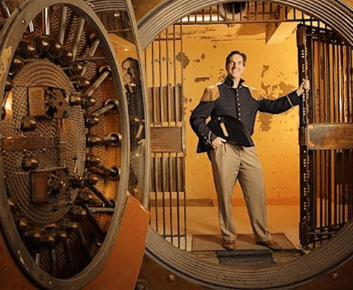 Man standing in a vault holding onto a barred gate