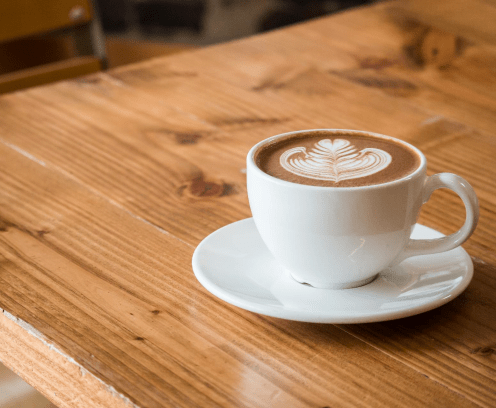Cup of coffee with milk froth decoration sitting on a saucer on a wooden table
