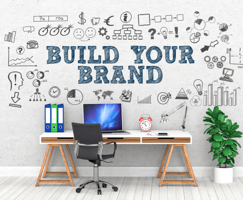 Build Your Brand written on wall above desk with laptop.