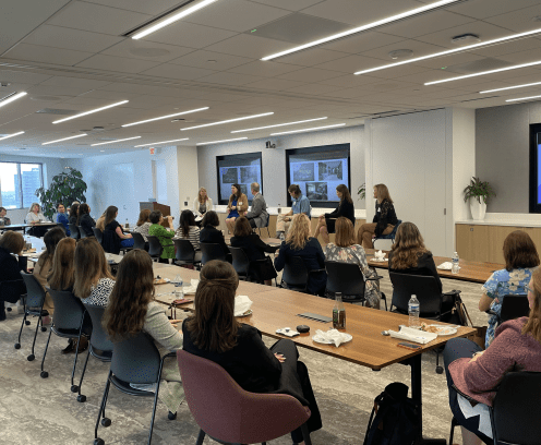 women sitting at tables in chairs with a panel speaking