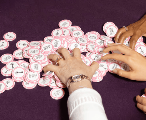 Diverse female hands reaching for pile of pink poker chips.