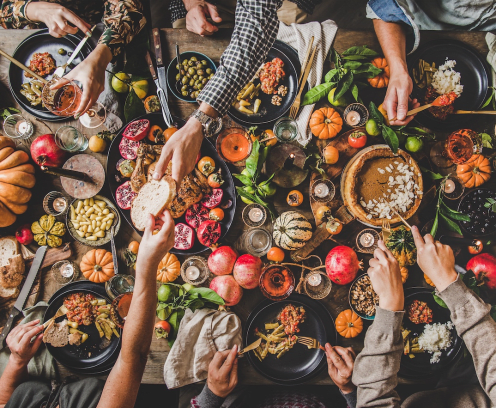 Table full of fall food and decor with hands passing bread, serving, and eating.