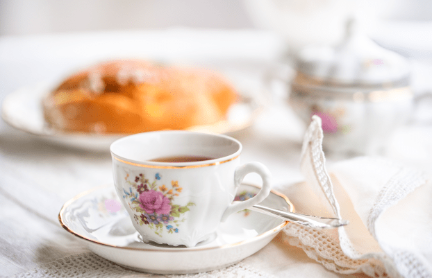 Luxury porcelain tea set with a cup, teapot, sugar bowl on white tablecloth with spongy cake on a plate