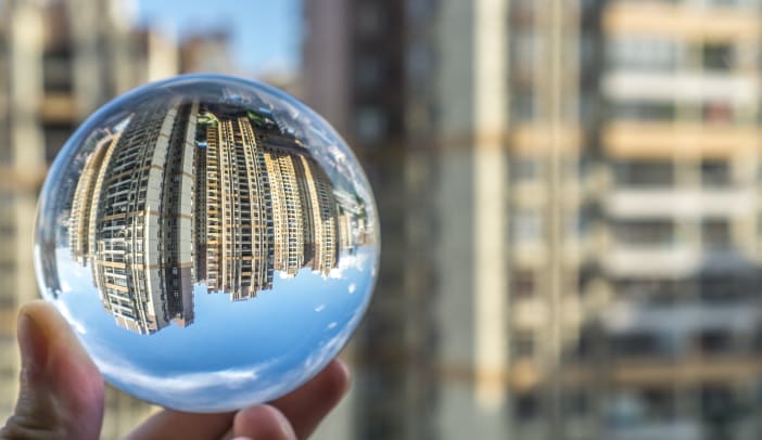 hand holding a glass ball reflecting city buildings in the background