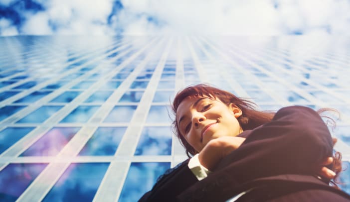businesswoman looking down at camera in front of glass skyscraper
